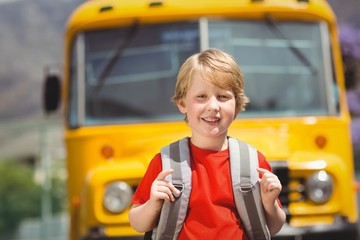 Cute pupil smiling at camera by the school bus