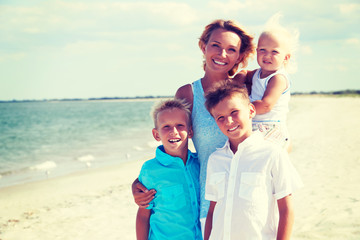 Smiling mother with children standing on the beach.
