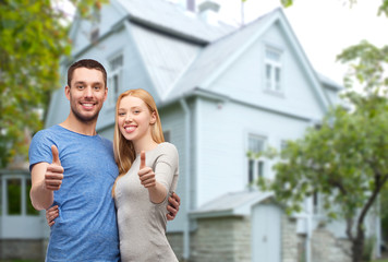 smiling couple showing thumbs up over house