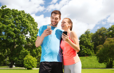 two smiling people with smartphones outdoors