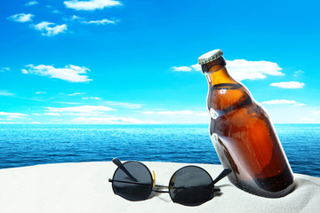 Obraz premium Bottle beer and sunglasses in the sand of a tropical beach