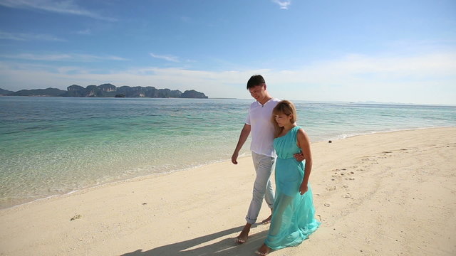 handsome man walk with asian blonde girl in blue dress on sandy 