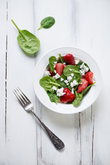 Salad with spinach, strawberry and cheese, white wooden surface