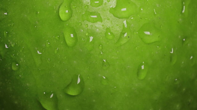 Drops of water flow down along the surface of a green apple
