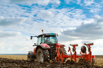 Farmer plowing stubble field with red tractor