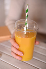 Female hand at wooden table with fast food closed cup of orange