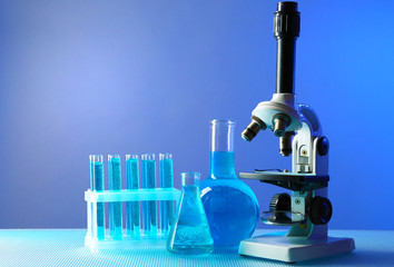 Microscope and test tubes on table, on color background