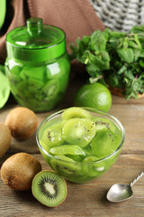 Tasty kiwi jam in glass bowl on wooden background