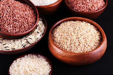 Different kinds of rice in bowls on wooden background