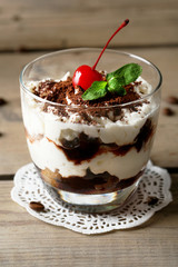 Tasty tiramisu dessert in glass, on wooden background