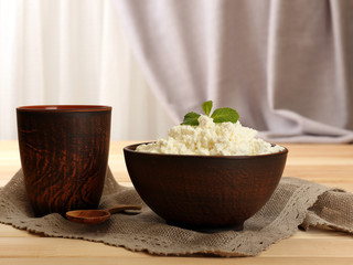 Cottage cheese in bowl with cup on table on fabric background