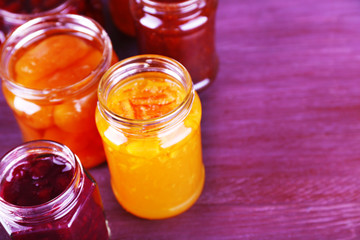Homemade jars of fruits jam on color wooden background