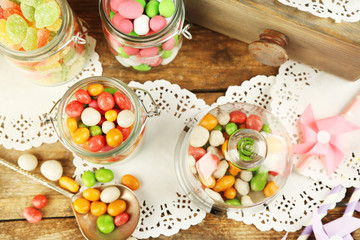 Multicolor candies in glass jars on wooden background