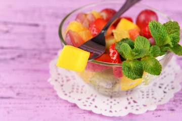 Fruit salad with mint in glassware on color wooden background
