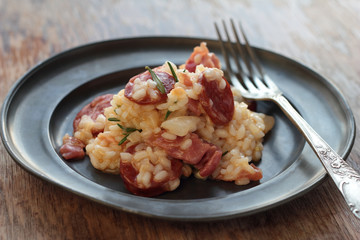 Risotto with sausage, cured ham and rosemary on a tin plate.