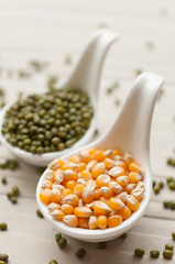 Yellow corn grain and mung beans in ceramic spoon on wooden back