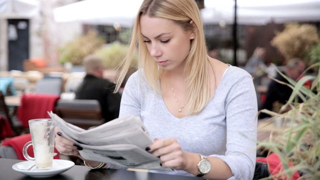 Attractive young woman is reading newspaper in cafe.FULL HD