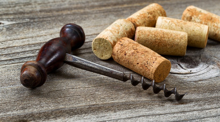 Old corkscrew with used corks in background on aged wood - obrazy, fototapety, plakaty