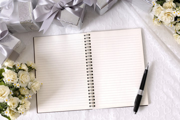 Wedding gifts and flowers on white lace background with blank open writing book for to do list