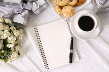 Wedding gifts and flowers on white lace background with biscuits coffee and blank open writing book for to do list