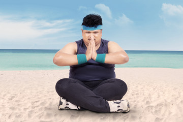 Overweight man doing yoga on beach 1