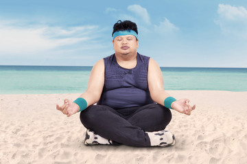 Overweight man doing yoga on beach