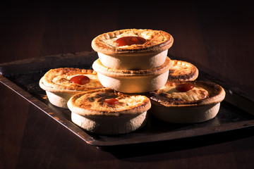 Freshly baked meat pies with sauce and high contrast lighting.