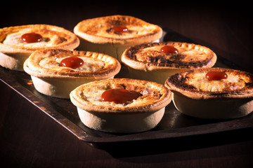 Freshly baked meat pies with sauce and high contrast lighting.