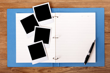 Desk with open blue project folder or photo album and blank polaroid style photo print frame