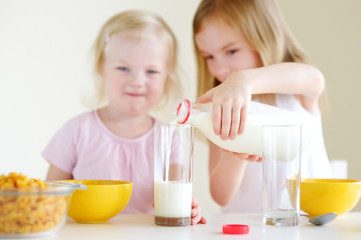 Two cute little sisters eating cereal in a kitchen
