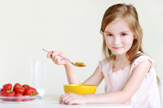 Adorable little girl eating cereal in a kitchen