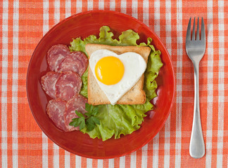 Fototapeta na wymiar Fried heart shaped egg on toast with salad and chorizo sausage f