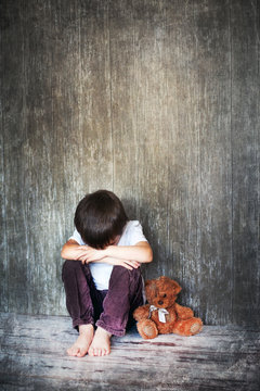 Young boy, sitting on the floor, teddy bear next to him, crying