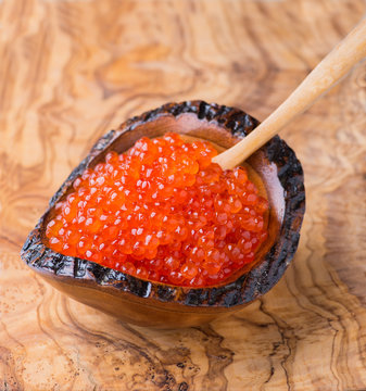 Red caviar in wooden bowl on olive wood background
