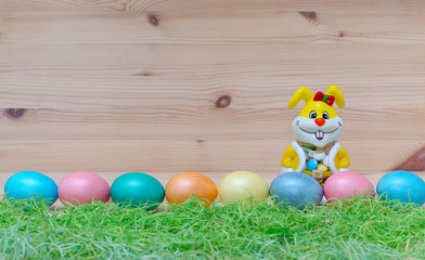 Fototapeta na wymiar happy bunny with easter eggs and grass on the wooden background
