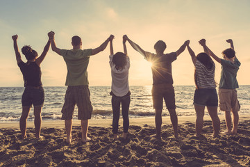Multiracial group of people with raised arms looking at sunset