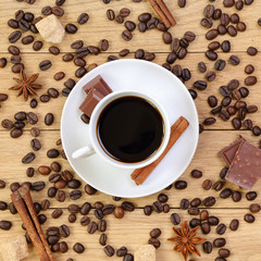 Cup of coffee, chocolate, sugar, spices and coffee beans on a wo