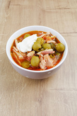Soup saltwort with lemon, meat, pickles, tomato sauce olives in a bowl on a sacking, bread on a wooden board background