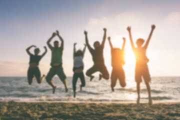 Group of people jumping at beach, blurred background.