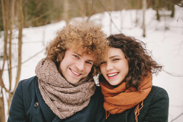 Portrait of young smiling couple with curly hair in winter fores