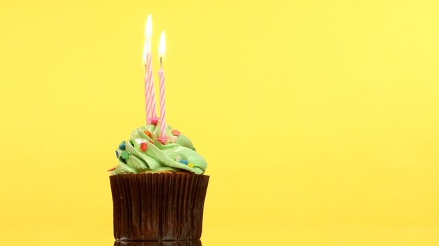 tasty birthday cupcake with three candle, on yellow background