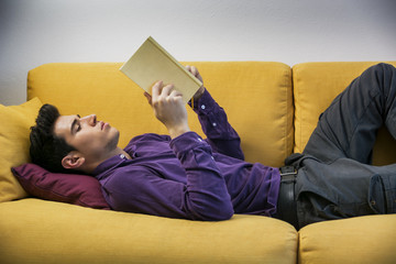 Handsome black haired young man reading book at home