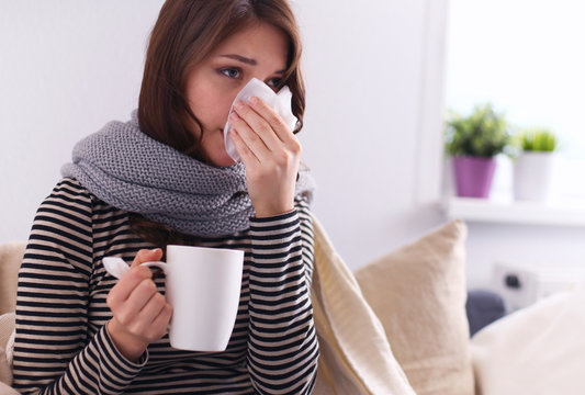 Sick woman covered with blanket holding cup of tea sitting on