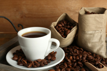 Cup of coffee with beans on tray and rustic wooden background