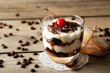 Tasty tiramisu dessert in glass, on wooden background