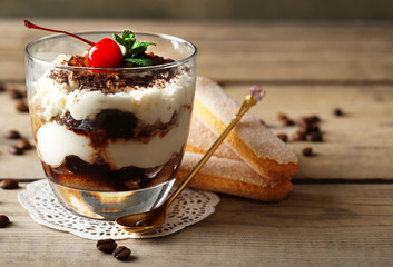 Tasty tiramisu dessert in glass, on wooden background