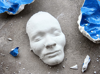 Plaster face mask in the middle of pieces of broken matt - 78613618