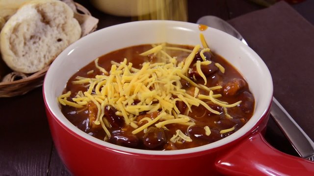 Sprinkling cheddar cheese on a bowl of chili