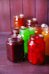 Homemade jars of fruits jam on color wooden background