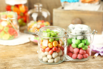 Multicolor candies in glass jars on wooden background